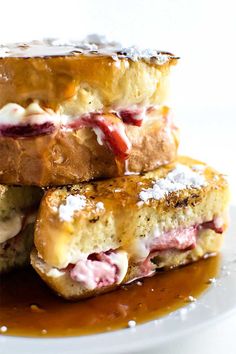 three sandwiches stacked on top of each other covered in jelly and powdered sugar, sitting on a white plate