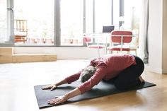 a woman is doing yoga on a mat in front of a large window with red chairs