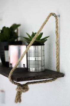 a metal can with rope hanging from it's side on a shelf next to a potted plant