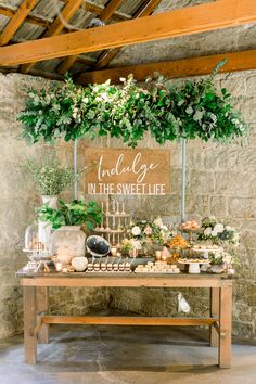 a wooden table topped with lots of food and greenery next to a sign that says indulge in the sweet life