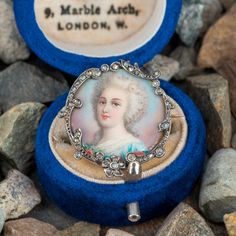 This wonderful silver topped, yellow gold, circa early Victorian era miniature portrait brooch features a hand painted portrait of a woman wearing a dress with flowers on the front. The brooch is accented with forty-two (42) bead set, rose cut diamonds. The brooch measures 24.4mm tall by 4.0mm thick and is finished with a pin stem and "C" catch. Dress With Flowers, Miniature Portraits, Portrait Of A Woman, Bead Set, Silver Tops, Kids Portraits, Rose Cut Diamond, Flower Dresses, Victorian Era