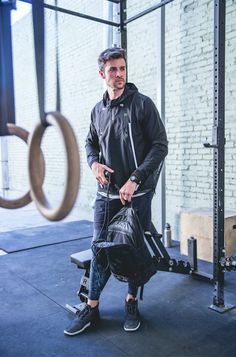 a man in black jacket holding a bag and standing next to a gym equipment rack