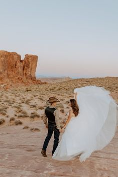 a bride and groom walking through the desert