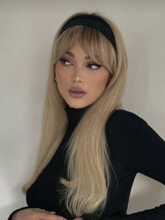 a woman with long blonde hair wearing a black dress and headband, standing in front of a white wall