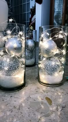 three glass vases filled with ornaments on top of a marble counter topped with lights