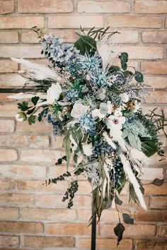 a bouquet of flowers and greenery on a stand in front of a brick wall