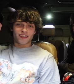 two young men sitting in the back seat of a car, one holding up his hand