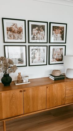 a wooden sideboard with pictures on the wall above it and vases filled with flowers