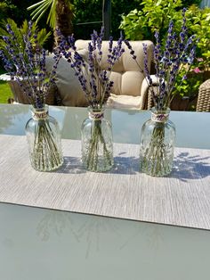 three glass vases filled with purple flowers on top of a table