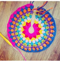 a colorful crocheted doily with a yellow knitting needle next to it on a wooden floor