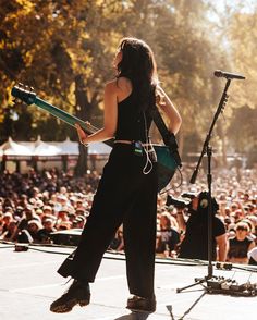 a woman holding a guitar while standing in front of a microphone on top of a stage