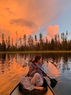 a woman is paddling in a canoe on the water at sunset or dawn,