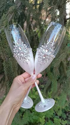 two champagne flutes being held up in front of a pine tree with lots of snowflakes on them