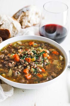 a white bowl filled with soup next to some bread and a glass of red wine