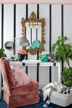 a room with black and white stripes on the walls, a pink chair, potted plants, and a gold framed mirror