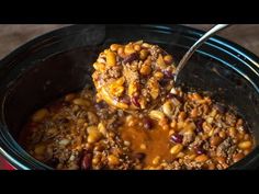 a ladle full of chili and beans in a crock pot with a spoon