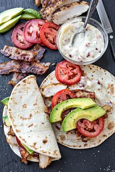 two tortillas with avocado, tomatoes and bacon are on the table