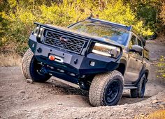 the truck is driving down the trail in the mud and rocks, with trees behind it