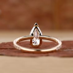 a gold ring with a pear shaped diamond in it's center, sitting on top of a piece of wood