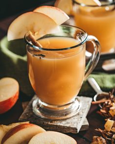 two glasses of apple cider on a table with apples and cinnamon sticks in the background