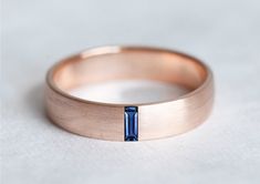 a rose gold band with a blue sapphire stone in the center, on a white surface