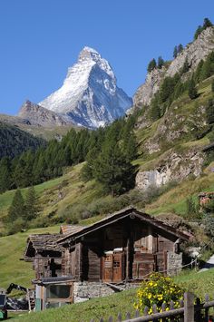 an old cabin in the mountains with a snow - capped mountain behind it