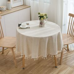 a white table with two wooden chairs and a vase filled with flowers sitting on top of it