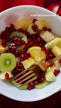 a white bowl filled with sliced fruit and pomegranates next to a fork