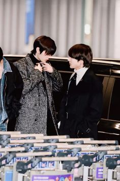 two young men standing next to each other in front of an airport baggage claim area