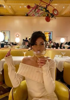 a woman sitting in a yellow chair holding a wine glass up to her face and looking at the camera