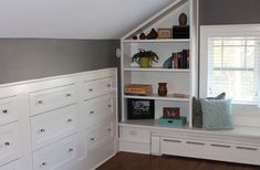 an attic bedroom with white cabinets and drawers