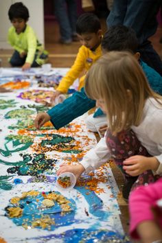 several children are painting on a large sheet of white paper with colorful paint and sprinkles