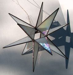 a stained glass star ornament hanging from a string on a white background with shadows