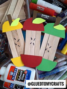 an apple cut out from popsicle sticks with glue on it and other crafting supplies in the background