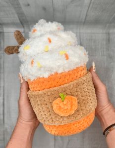 someone is holding up a crocheted cupcake with whipped cream and orange icing