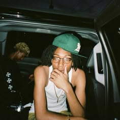 a man sitting in the back seat of a car wearing a green hat and glasses