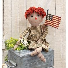 a doll sitting on top of a suitcase with an american flag hanging from it's side