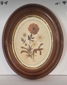 a brown frame with flowers on it is hanging on the wall in front of a white wall