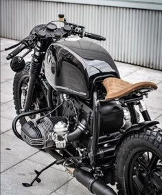 a black motorcycle parked on top of a cement floor next to a building with a brown leather seat