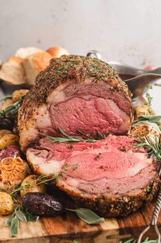 roast beef with herbs and spices on a wooden cutting board next to bread, potatoes and olives