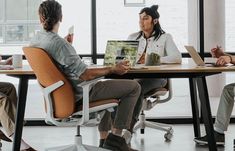 three people sitting at a table with laptops and papers in front of them, talking