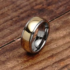 a gold and black wedding ring on top of a wooden table with wood inlays