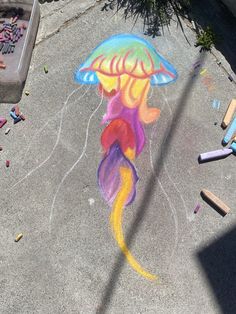 a child's chalk drawing of a jellyfish on the ground next to crayons