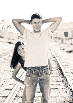 a man and woman standing next to each other in front of train tracks with their hands on their head