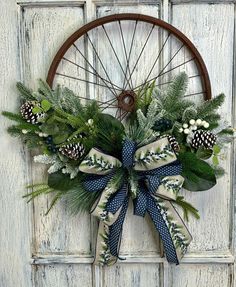 a wreath with pine cones and evergreen leaves on a door hanger in front of an old wheel