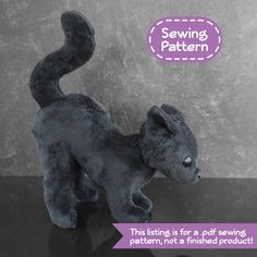 a gray stuffed animal cat sitting on top of a black table next to a sign that says sewing pattern