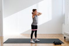 a woman standing on a yoga mat with her hands behind her head