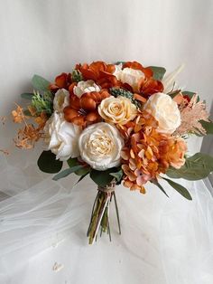 a bridal bouquet with orange, white and brown flowers on a white cloth background