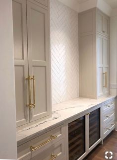 an empty kitchen with marble counter tops and gold pulls on the cabinets, along with wine bottles