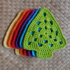 four crocheted dishcloths are sitting on a woven mat, one is green and the other is multicolored